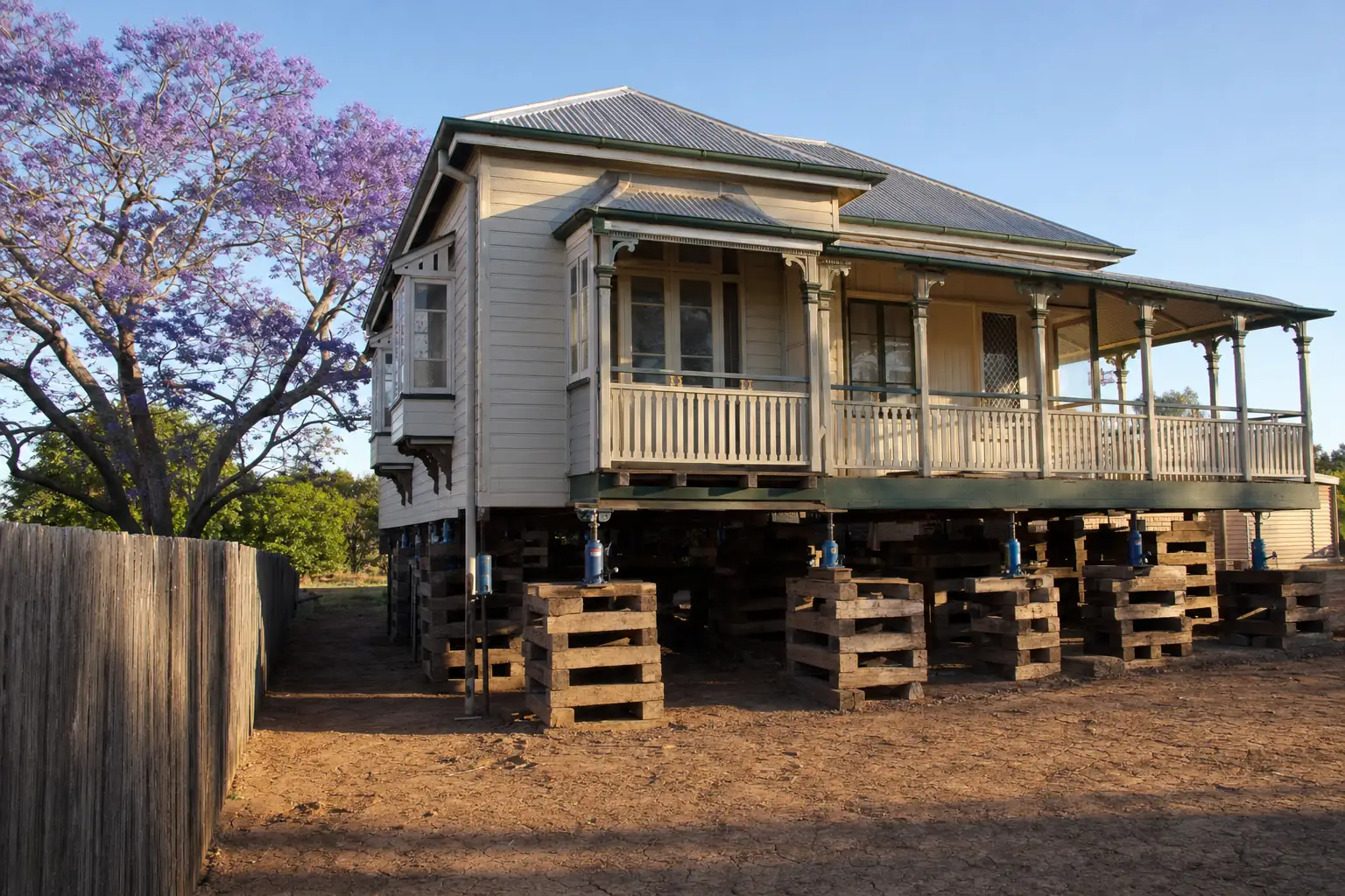 Queenslander house raised on hardwood cribbing with hydraulic jacks, jacaranda tree beside it, illustrative example